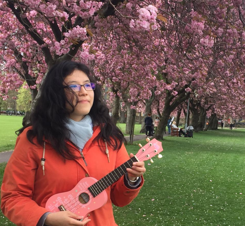 Photo of woman singing with a ukelele under trees with cherry blossom